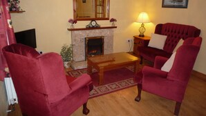 A living room with a fireplace, two red armchairs, a wooden coffee table, a lamp, and a framed picture on the wall. - Lakeside Lodge Bantry (Bantry)