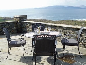 Une table ronde avec deux chaises, une bouteille de vin et deux verres à vin, le tout placé sur une terrasse donnant sur la mer.