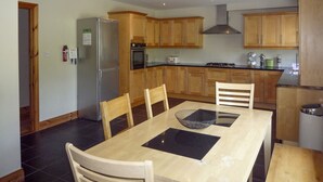 Une cuisine moderne avec des meubles en bois, un réfrigérateur en acier inoxydable, un four et une cuisinière à gaz. On y trouve une table à manger avec des chaises et un set de table noir.