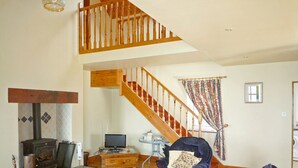 A spacious living room with a wooden staircase, a fireplace, and comfortable seating. - Allaghee Mor St. Finian's Bay (Ballinskelligs)