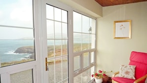 A room with a large sliding glass door leading to a scenic ocean view, a red chair, and a framed picture on the wall. - Allaghee Mor St. Finian's Bay (Ballinskelligs)