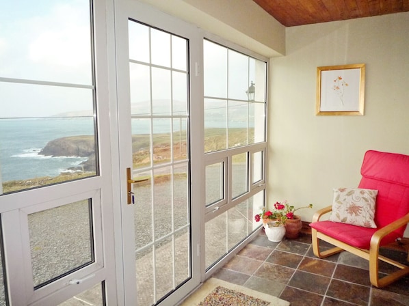 A room with a large sliding glass door leading to a scenic ocean view, a red chair, and a framed picture on the wall.