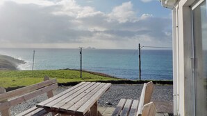 A wooden bench and table on a gravel patio with a view of the sea and distant land. - Allaghee Mor St. Finian's Bay (Ballinskelligs)