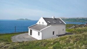 A white house with a sloped roof and a small porch, situated on a grassy hill overlooking the sea. - Allaghee Mor St. Finian's Bay (Ballinskelligs)