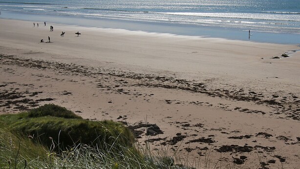 Ein Strand mit Menschen, darunter Surfer, und Bergen im Hintergrund.