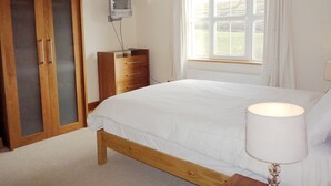 Ein Schlafzimmer mit einem hölzernen Bett, einem Schminktisch, einem an der Wand befestigten Fernseher und einem Fenster mit Vorhängen.
