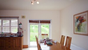Ein Essbereich mit Holztisch und -stühlen, eine Küche mit Schränken und einem Fenster sowie eine Tür, die nach draußen führt.