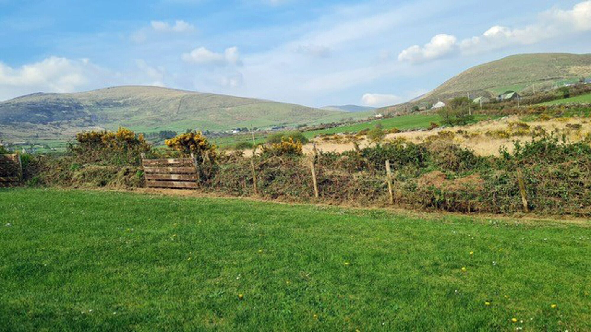 A rural landscape with a grassy field, a wooden fence, and distant hills.