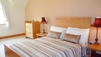 A bedroom with a large bed, a nightstand, a dresser, and a lamp.