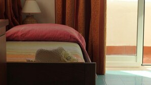 A bedroom with a bed, a nightstand, a lamp, and a view of the outside.