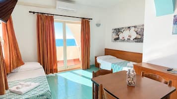 A hotel room with a bed, a desk, and a chair. There is a window with curtains, a flat-screen TV mounted on the wall, and a small table with a jar on it.