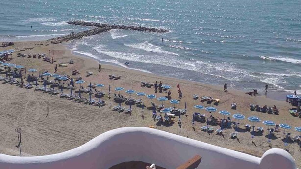 A beach with rows of sunbeds and umbrellas, a rocky breakwater, and the ocean.