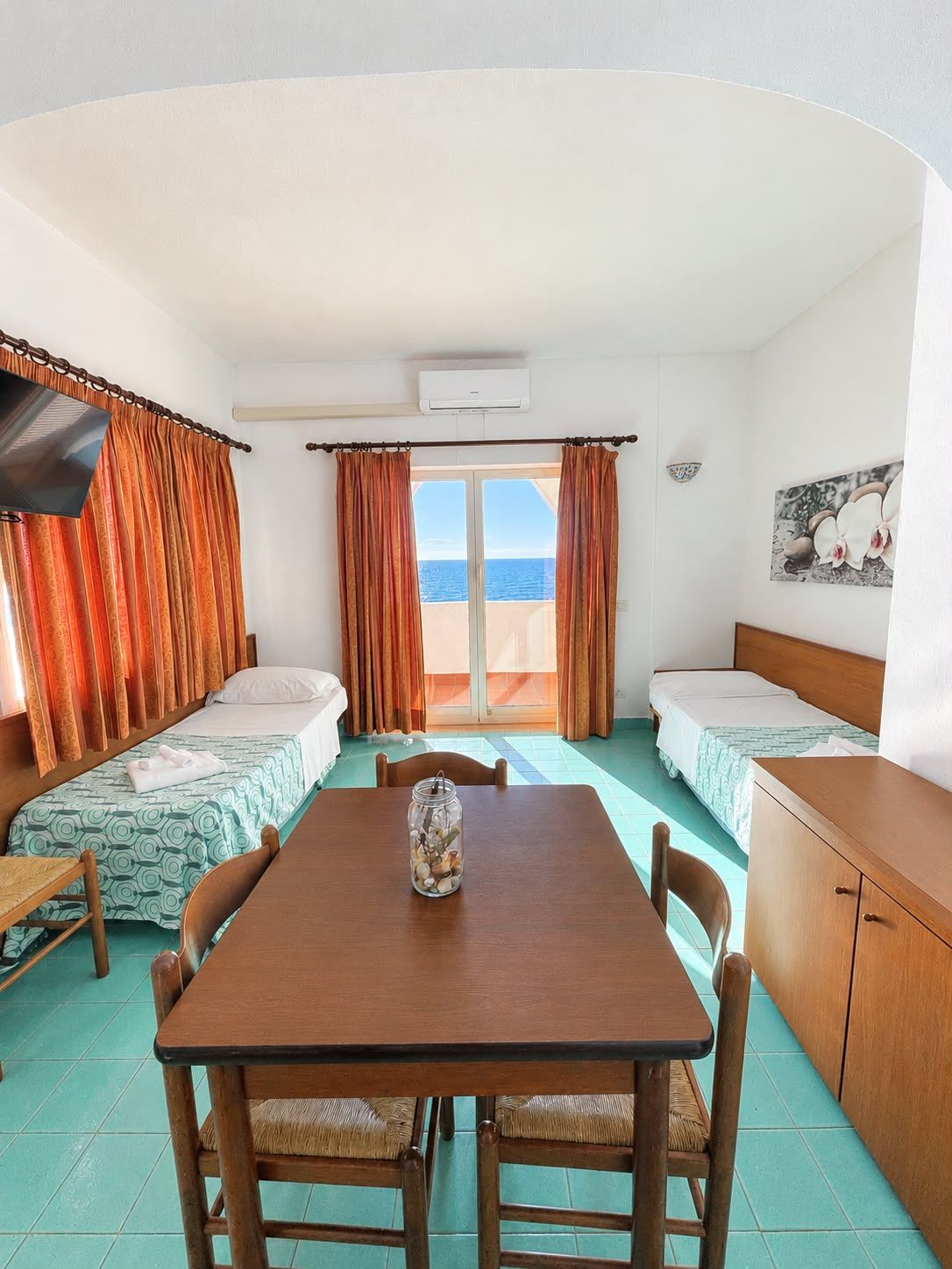 Une chambre avec deux lits, une table, des chaises, un téléviseur et une vue sur la mer.
