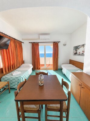 Une chambre avec deux lits, une table, des chaises, un téléviseur et une vue sur la mer.
