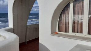 A balcony with a view of the ocean, a white table, and a white chair.