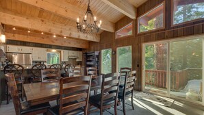 A wooden interior with a dining table and chairs, a chandelier, and large windows offering views of the outdoors. - Chamberlands Cabin: 5  BR, 3  BA House in Tahoma, Sleeps 10 (Tahoma)