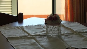A table with a lace tablecloth, a glass vase with flowers, and a view of the beach through a window. - Two-room apartment, terrace, sea front, floor 1 (Mimosa) (Anzio)