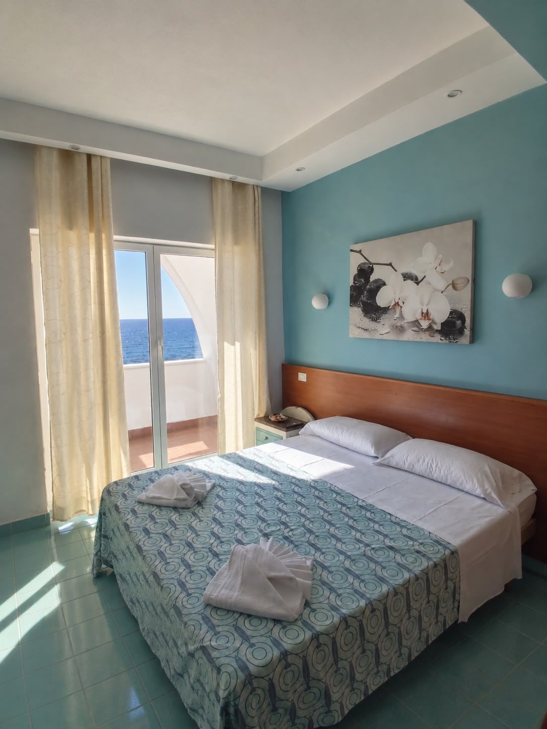 Una camera d'albergo con un letto, un comodino, un quadro e vista sul mare.