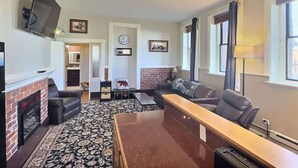 A living room with a fireplace, a television, a sofa, a coffee table, and a lamp. - Papa's Place — Historic 1BR Brick Unit, Walk to Main St Leadville (Leadville)