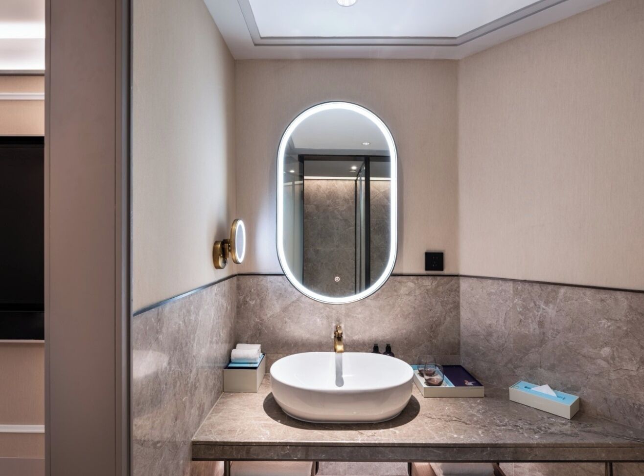 Un baño moderno con un espejo redondo, un lavabo y una encimera de mármol.