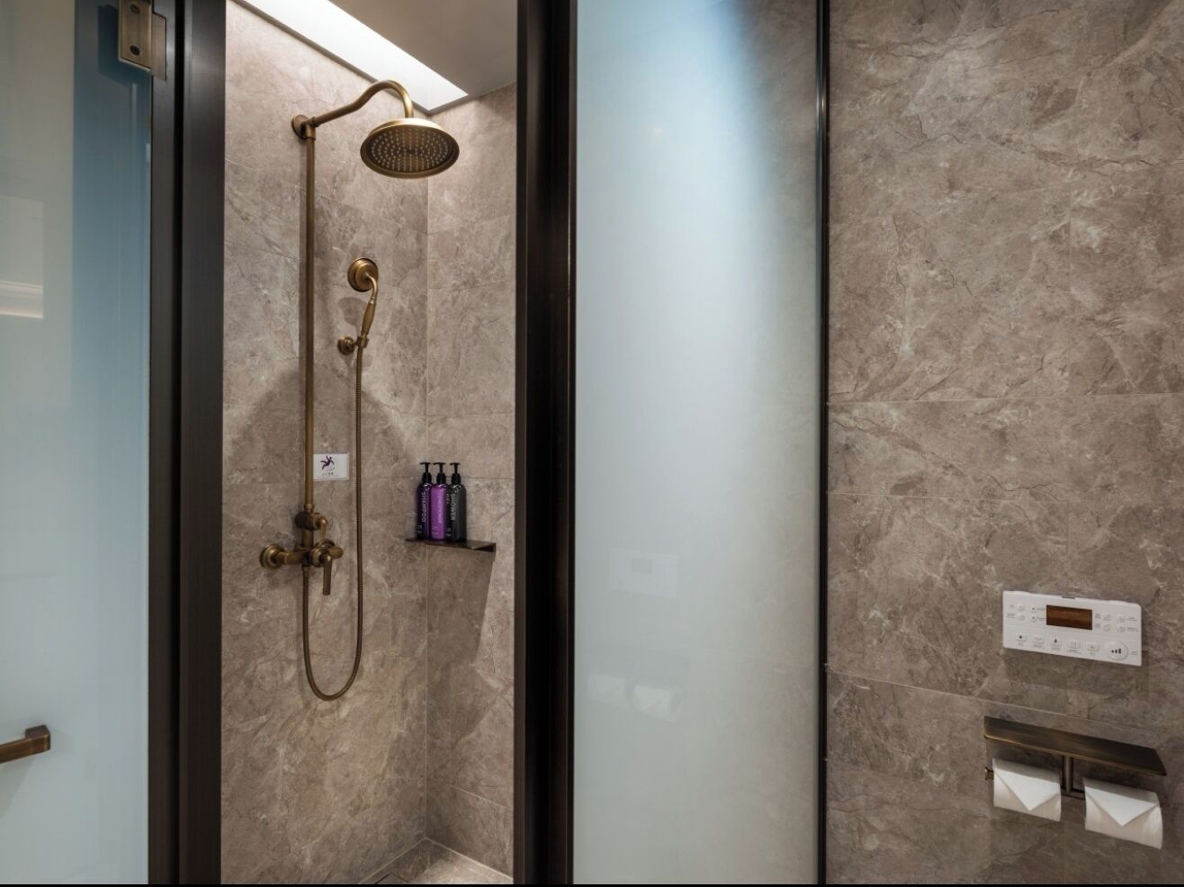 A modern bathroom with a shower, a control panel, and a shelf with toiletries.