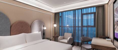 Una habitación de hotel con una cama grande, dos sillones, una mesita y un televisor.