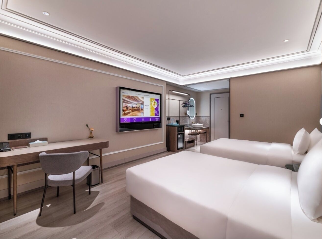 A modern hotel room with a bed, desk, chair, TV, and a small bathroom area.