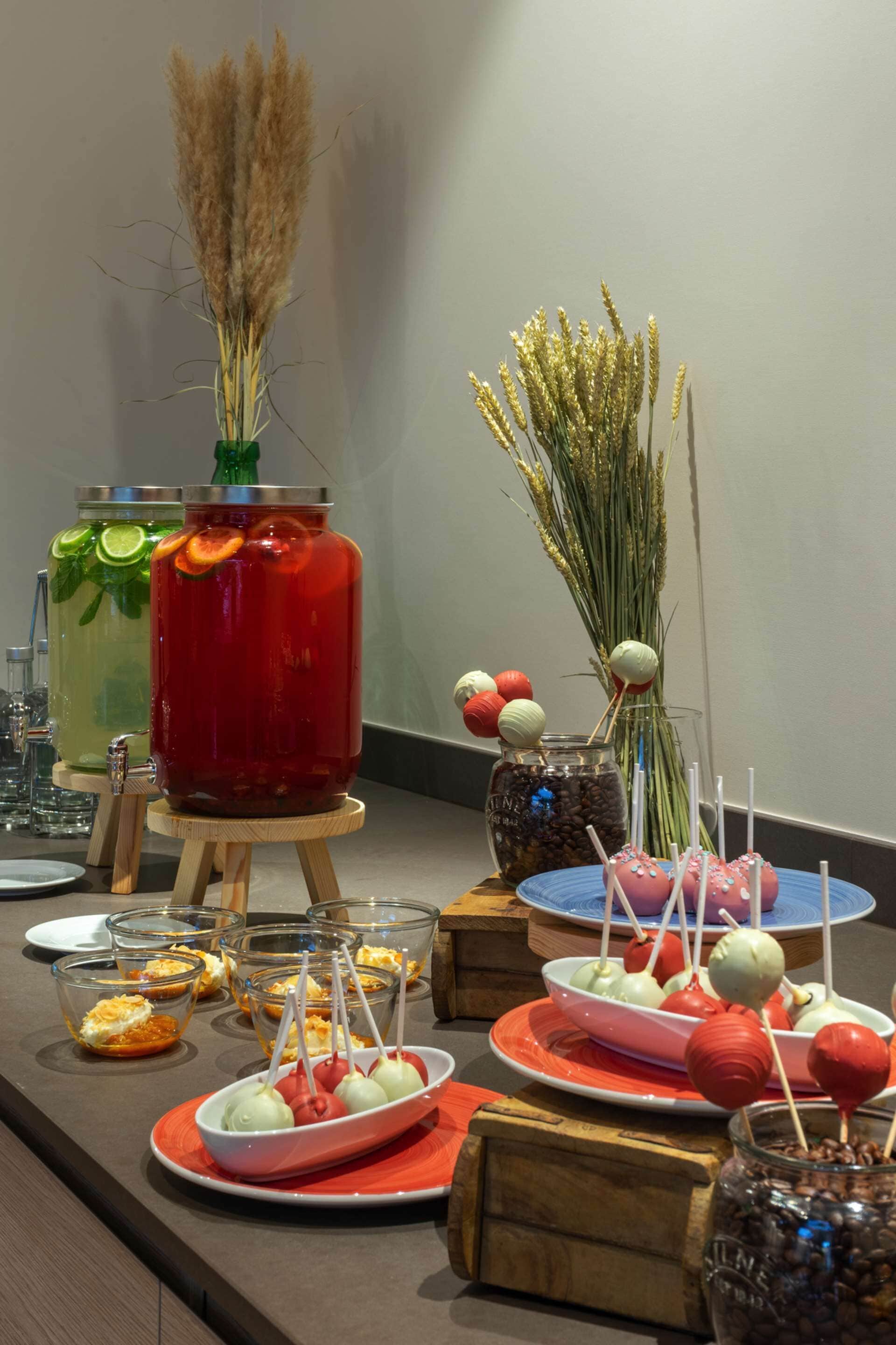 Una mesa de buffet con diversos alimentos y bebidas, incluyendo frascos con bebidas y platos de postres.