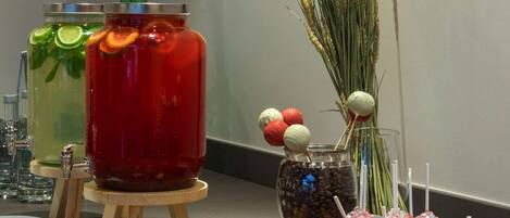 Una mesa de buffet con diversos alimentos y bebidas, incluyendo frascos con bebidas y platos de postres.