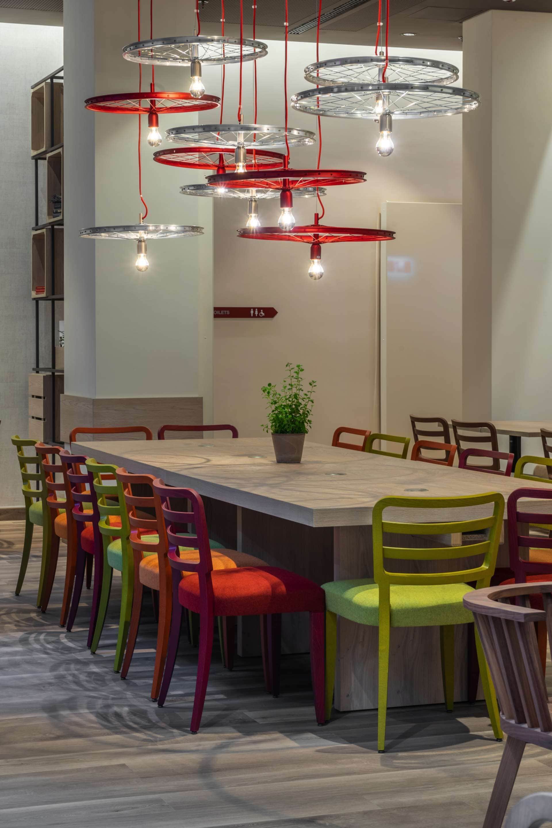 A modern dining area with a long table, colorful chairs, and unique circular pendant lights.