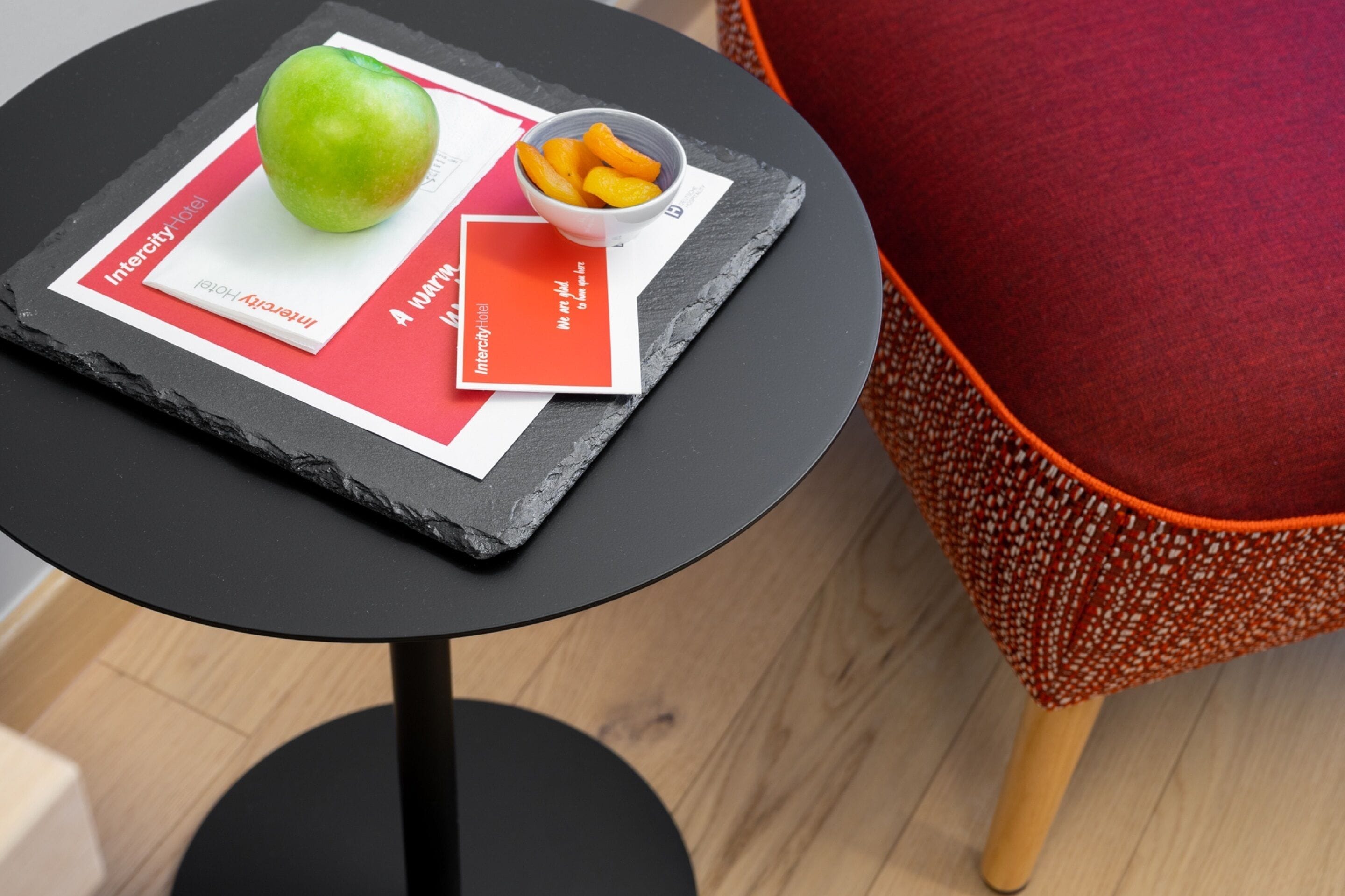 A round black table with a placemat, a green apple, and a bowl of orange slices.