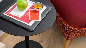A round black table with a placemat, a green apple, and a bowl of orange slices.