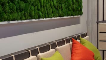 A row of beige sofas with colorful cushions, a green moss wall, and a wooden cabinet to the right.