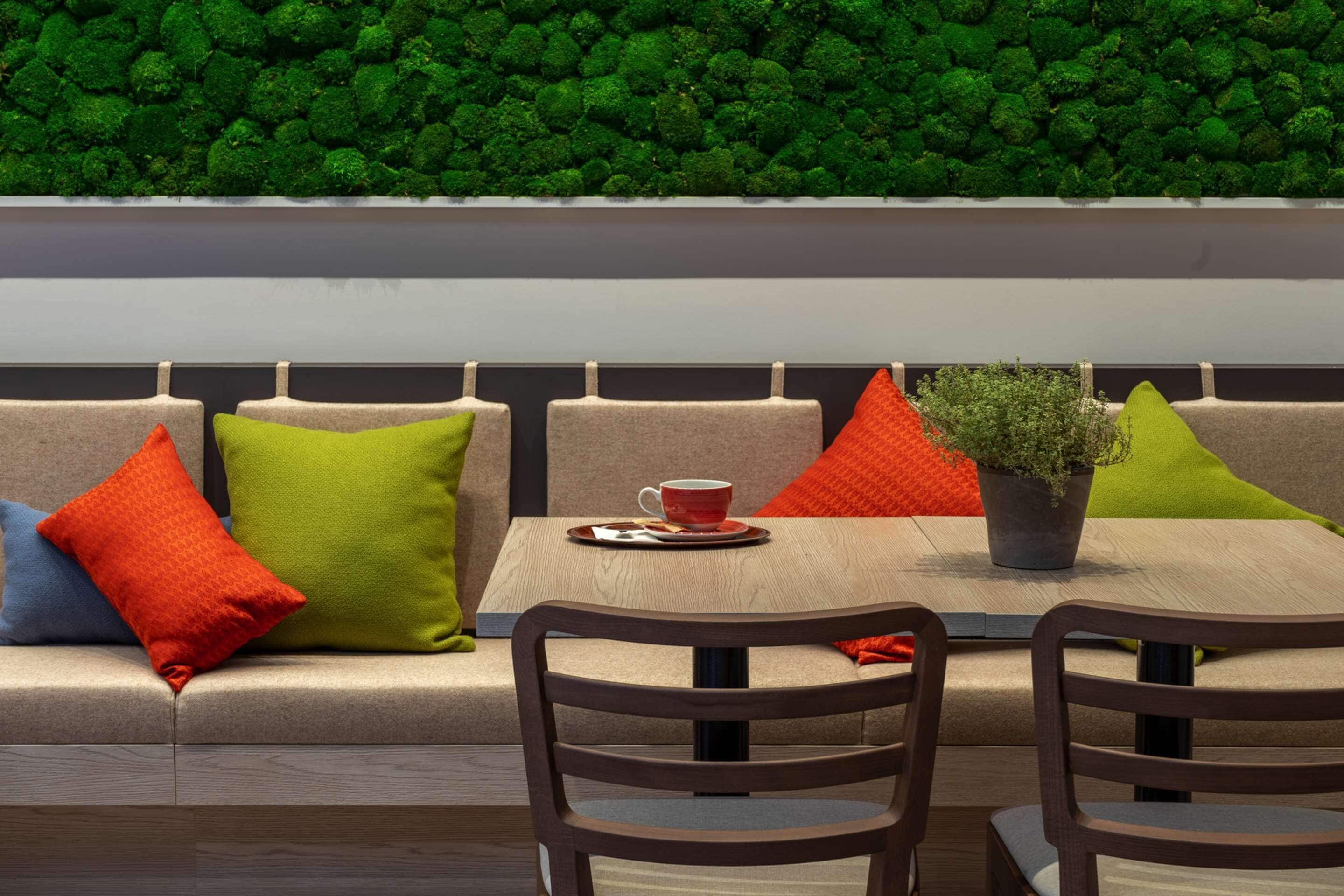 Ein moderner Sitzbereich mit einer Couch, zwei Sesseln, einem Tisch mit roter Tasse und Untertasse sowie einer Topfpflanze.