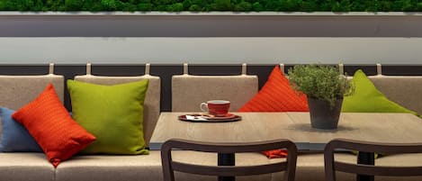 Un área de estar moderna con un sofá, dos sillones, una mesa con una taza y un platillo rojos, y una planta en maceta.