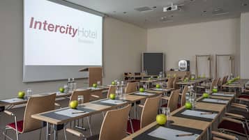 Ein Konferenzraum im Intercity Hotel Budapest mit Tischen, Stühlen und einer Projektionsleinwand, auf der der Hotelname zu sehen ist.