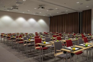 Un salón de conferencias con mesas y sillas dispuestas en filas, equipado con proyectores e iluminación del techo.