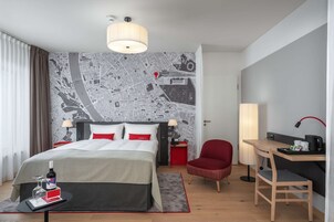 Habitación de hotel con una cama grande, un escritorio, una silla, papel tapiz con un mapa y una pared de acento roja.