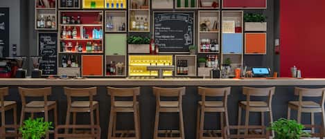 Una zona de bar con varias estanterías llenas de botellas, un menú en la pizarra y sillas de madera.