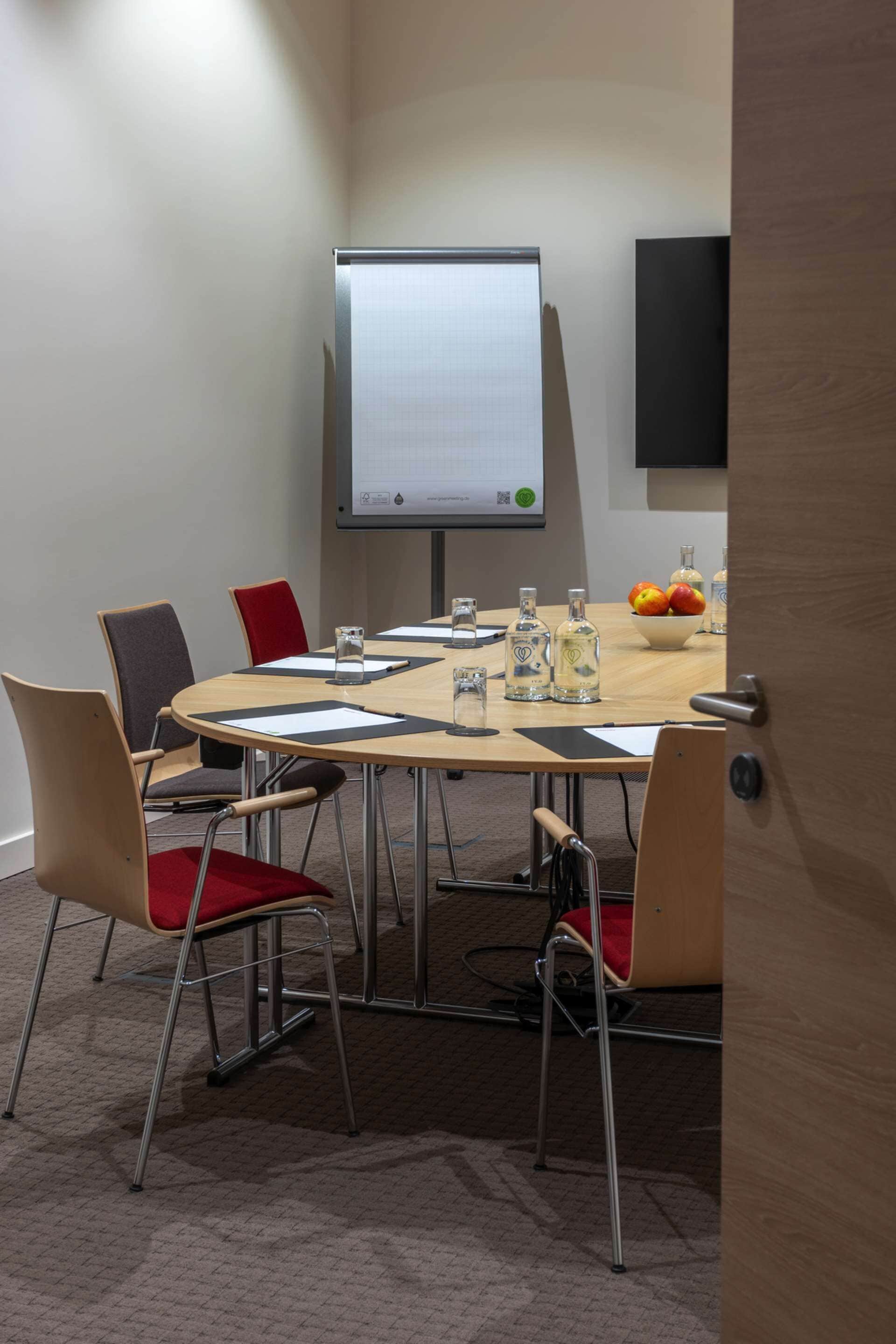 Una sala de conferències amb una taula rodona, sis cadires, una pantalla de projector i un plat de fruita.