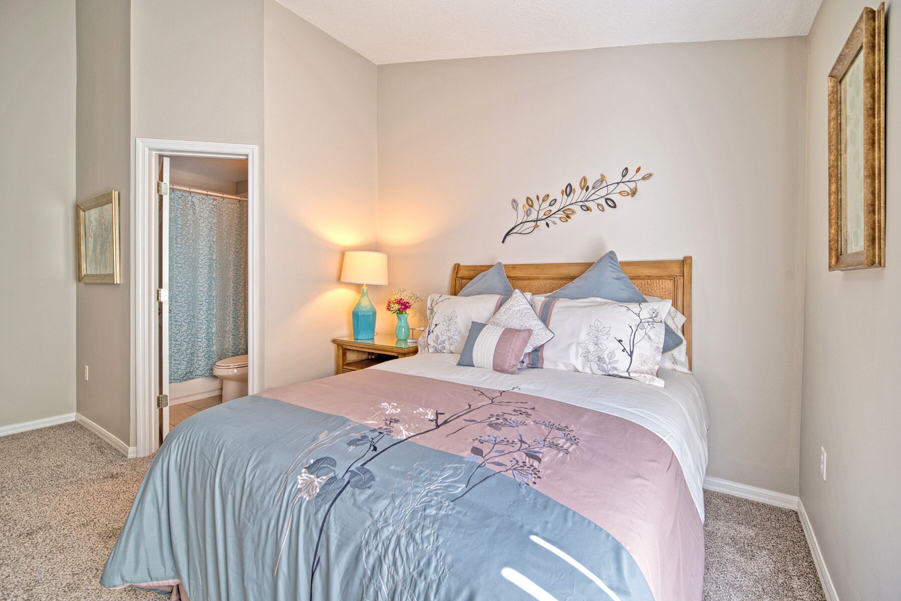 A bedroom with a bed, a nightstand, a wall-mounted mirror, and a door leading to another room.