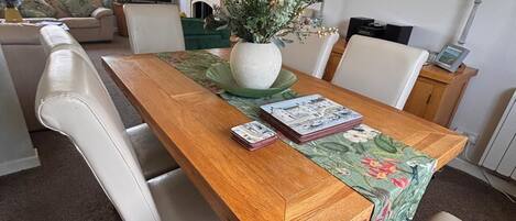 A dining area with a wooden table, white chairs, a green table runner, and a vase with flowers.