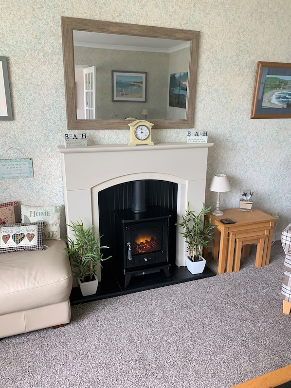 A cozy living room with a fireplace, a mirror above it, and a small table with a lamp. - Osborne Cottage (Campbeltown)