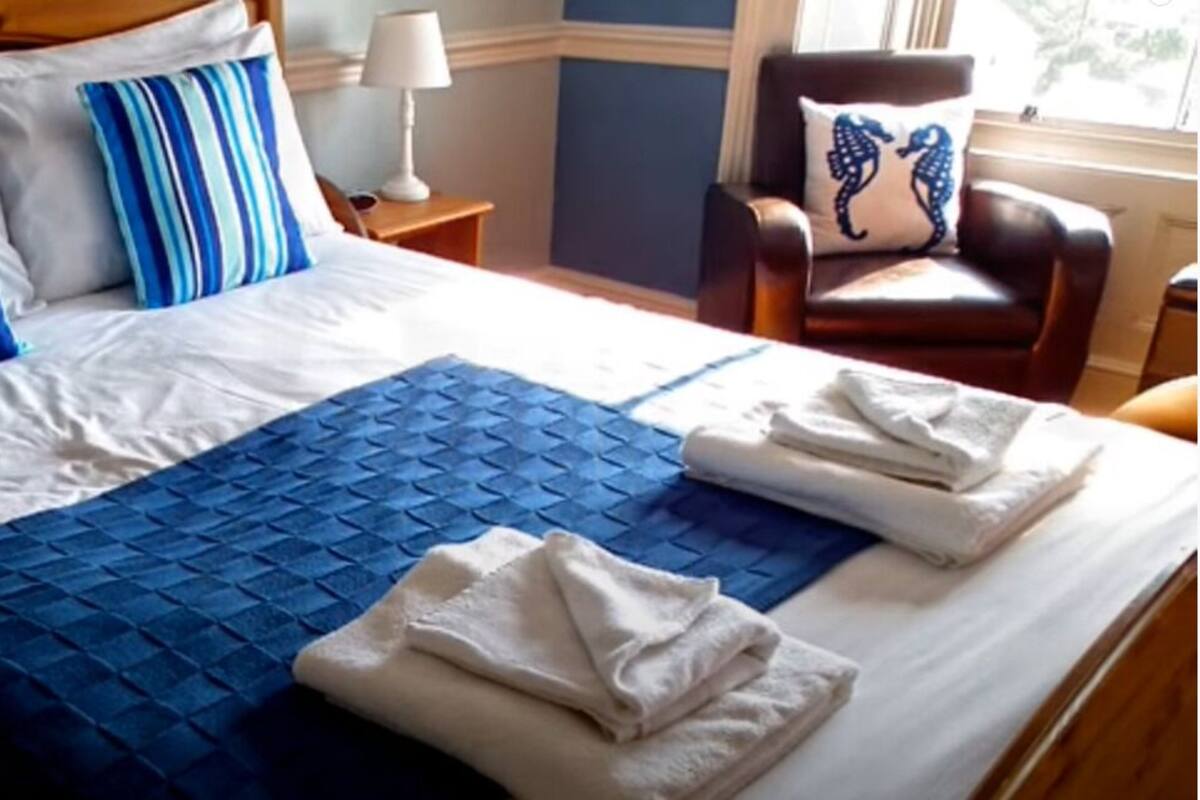 A neatly made bed with blue and white bedding, a blue quilt, and folded towels.