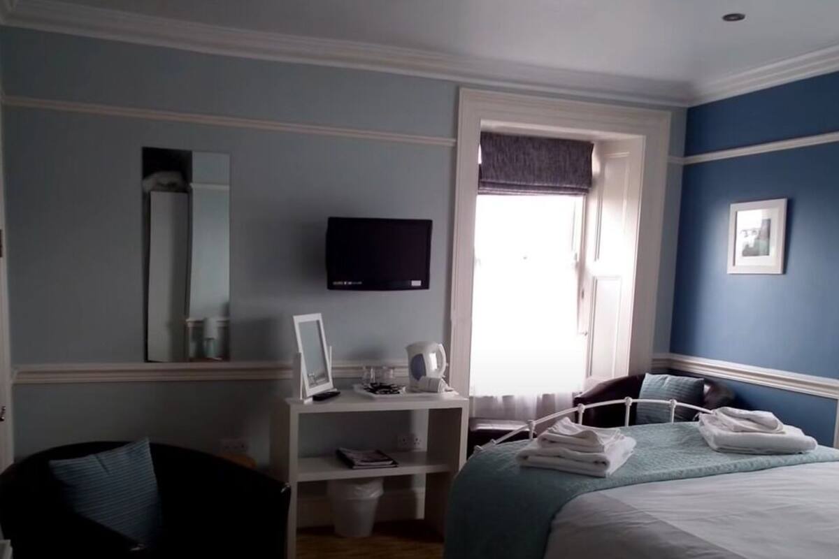 A bedroom with a bed, a desk, a chair, a television, and a window.