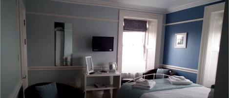 A bedroom with a bed, a desk, a chair, a television, and a window.