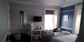 Un dormitorio con cama, escritorio, silla, televisor y ventana.