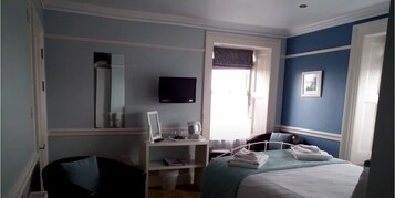 Un dormitorio con cama, escritorio, silla, televisor y ventana.