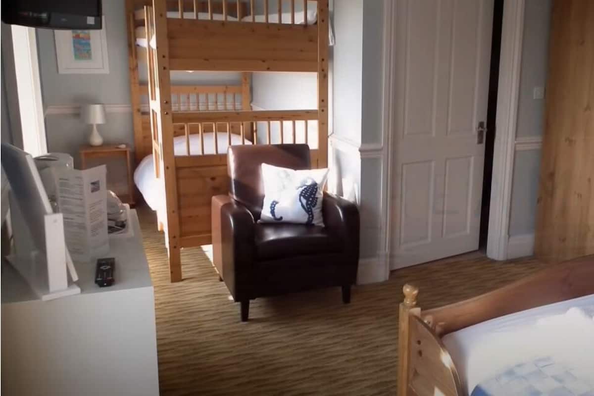 A bedroom with a bunk bed, a leather chair, a bed with towels, a wooden wardrobe, and a small bedside table.