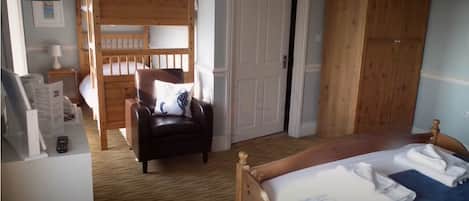 A bedroom with a bunk bed, a leather chair, a bed with towels, a wooden wardrobe, and a small bedside table.